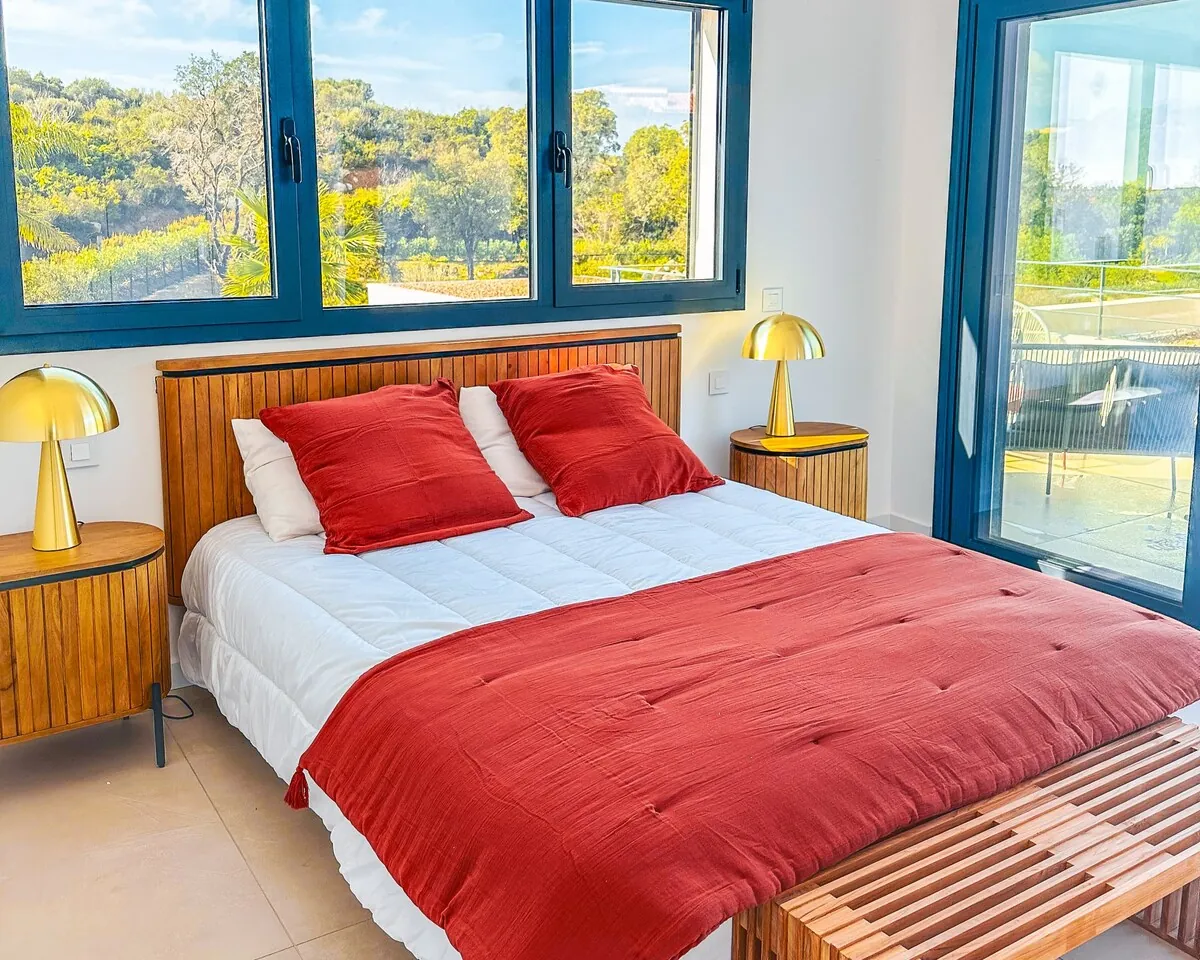 Chambre avec lit double, grandes fenetres et linge rouge.