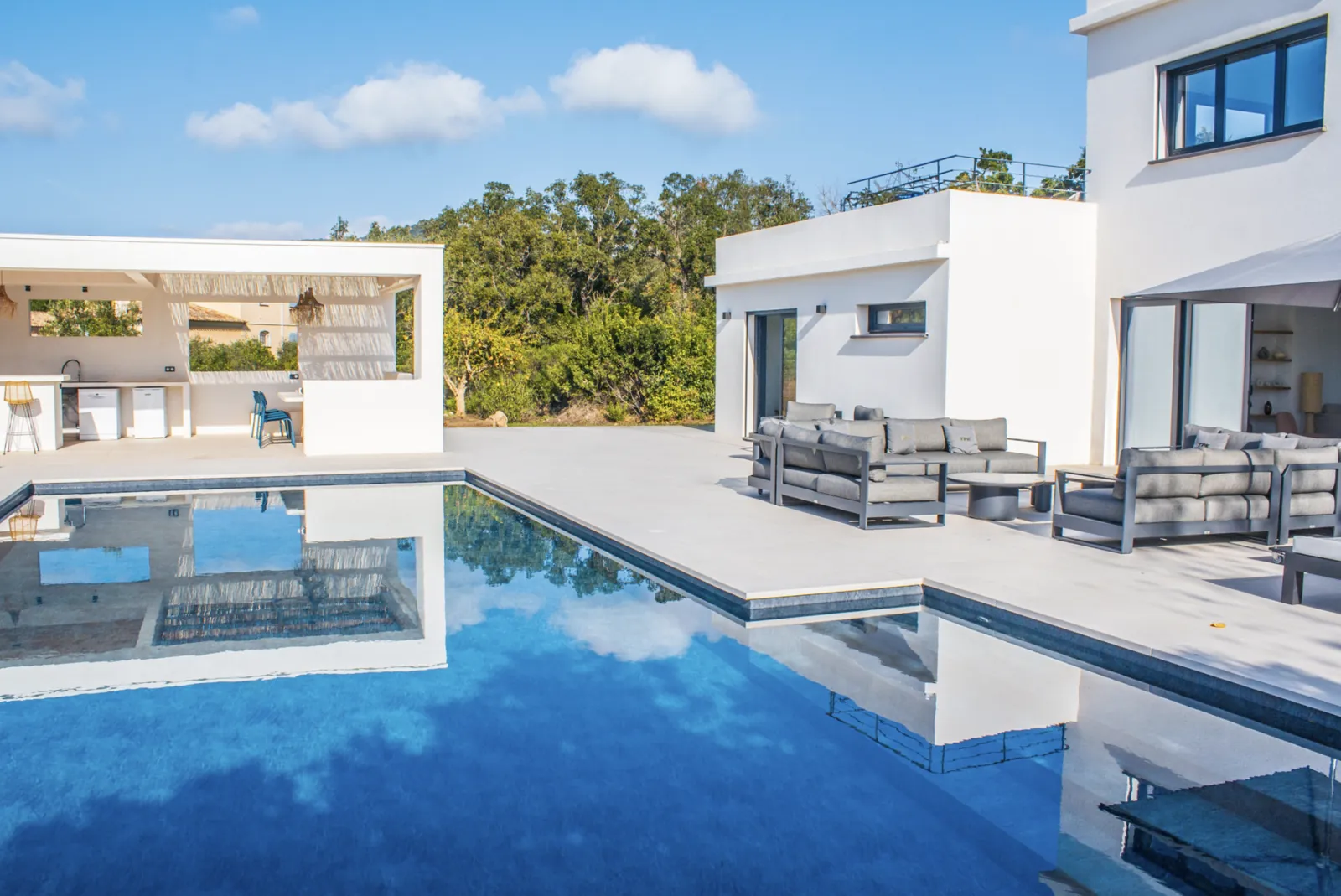 Salon exterieur avec canapes et table basse face a la piscine.